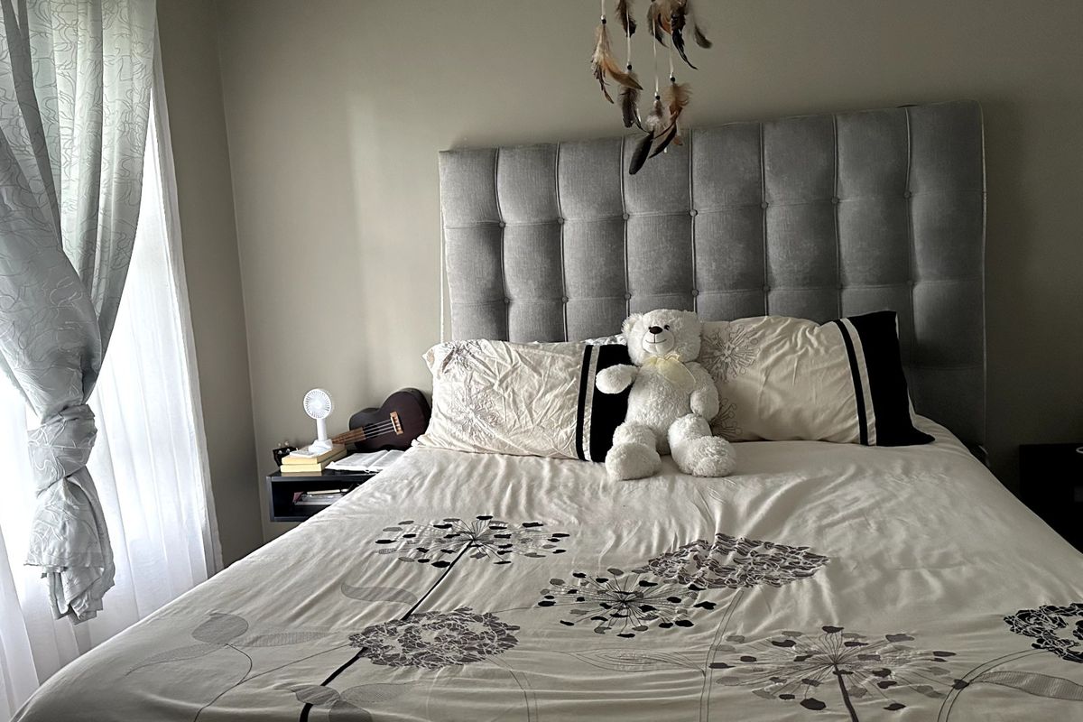 A comfortable bedroom featuring a large, grey upholstered headboard and natural light from the adjacent window.
