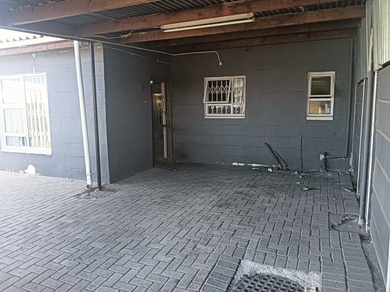 A covered carport area featuring paved flooring, security-fitted windows, and direct access to the property entrance.