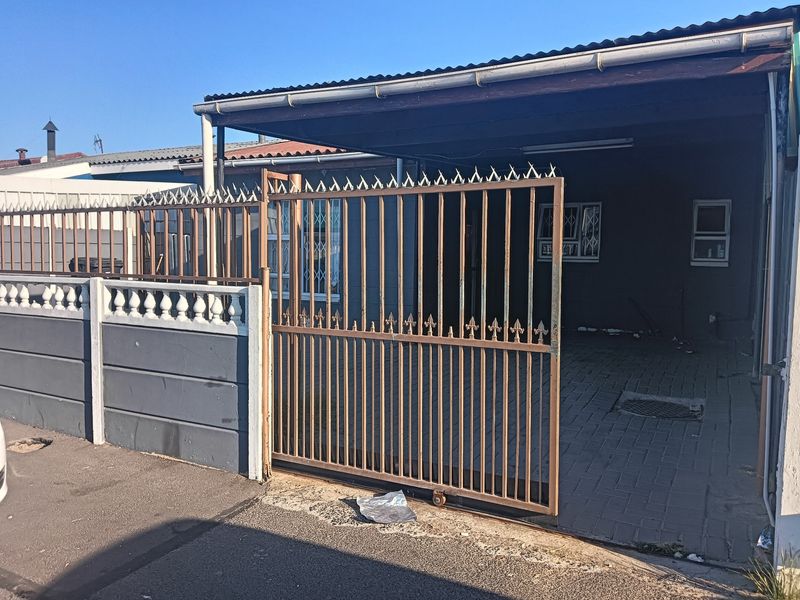 Front exterior view of a cluster property featuring a paved driveway, carport, and secure perimeter fencing with a sliding gate.