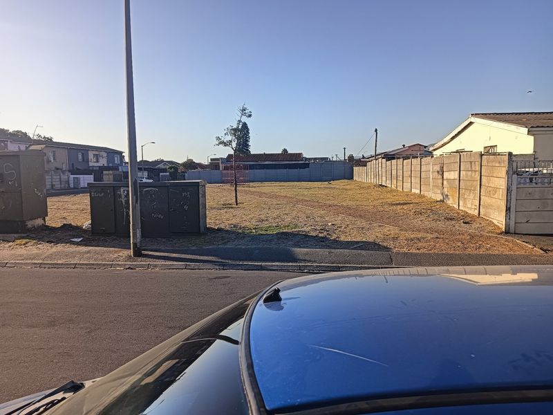 A vacant plot of land featuring a precast concrete boundary wall and electrical utility infrastructure, viewed from the street.