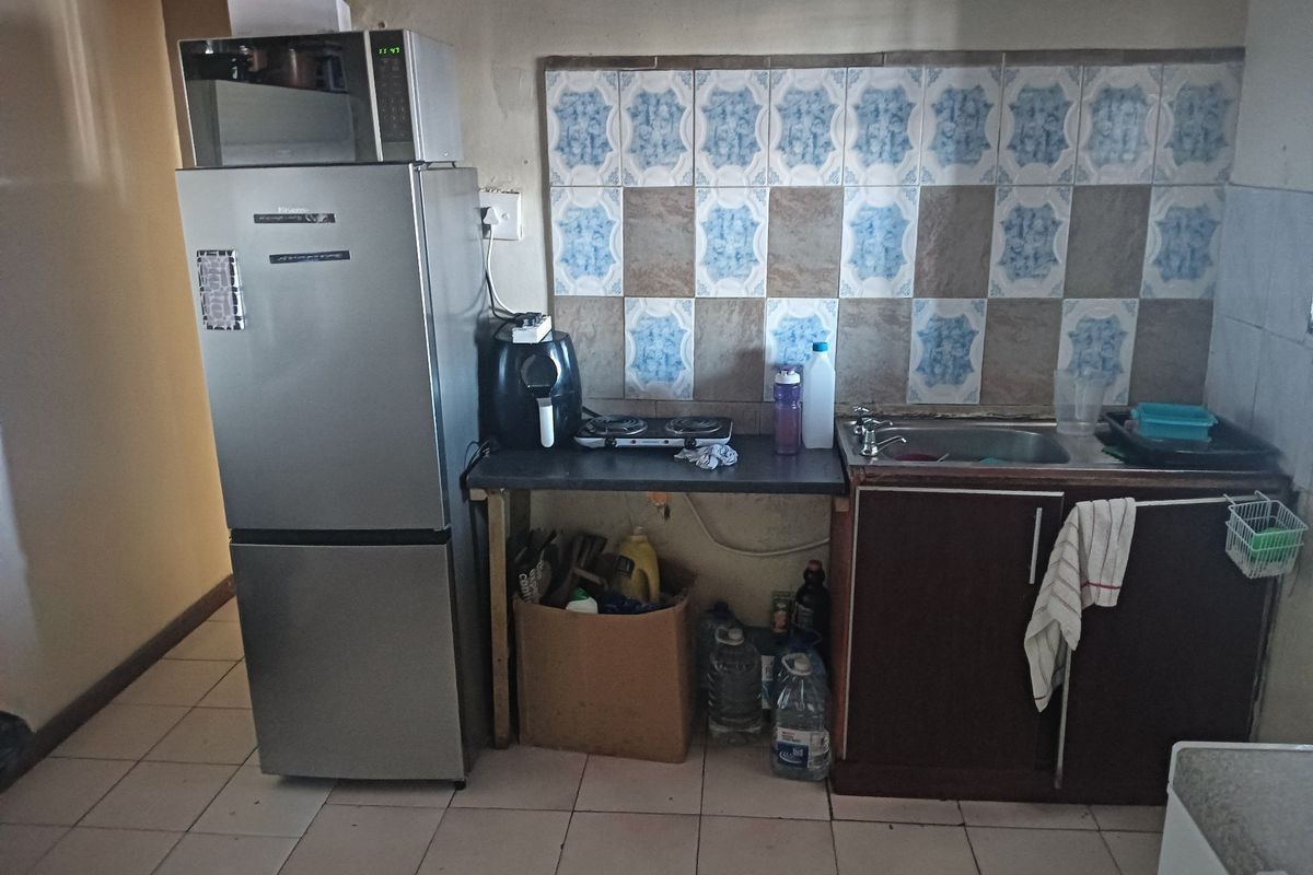 A compact kitchen area featuring a tiled backsplash, basic base cabinetry, and a single sink, requiring modernization to improve functionality and aesthetic appeal.