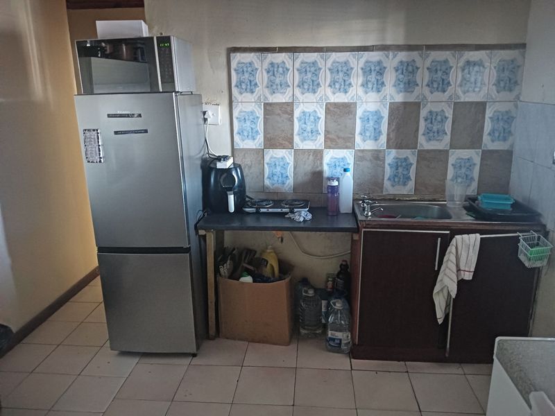 A compact kitchen area featuring a tiled backsplash, basic base cabinetry, and a single sink, requiring modernization to improve functionality and aesthetic appeal.