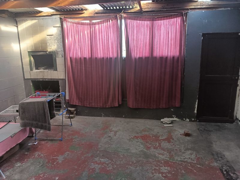 An unfinished, enclosed patio area featuring a built-in braai, exposed roof structure, and worn concrete flooring, requiring significant renovation and repair.