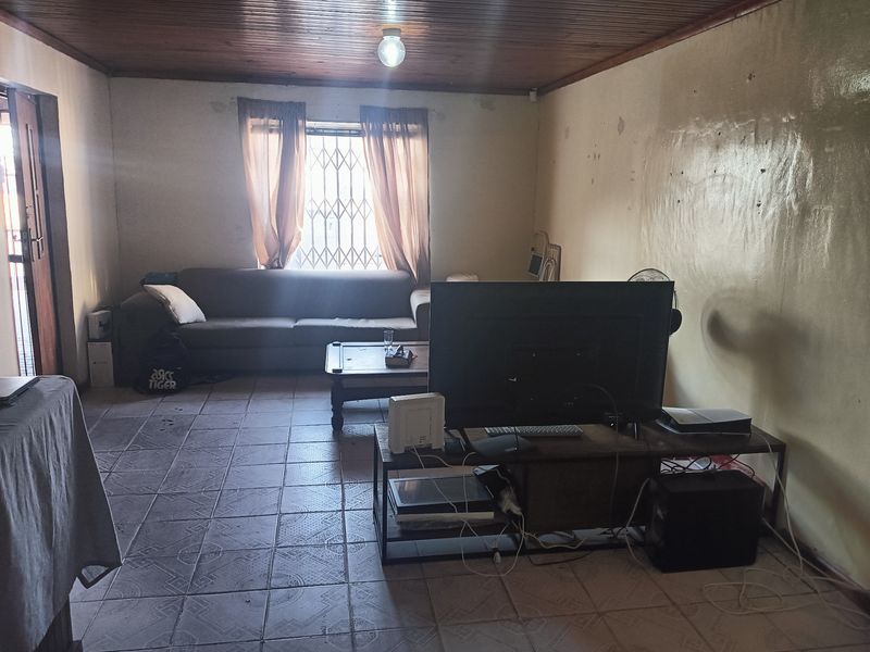 A living room featuring tiled flooring and a timber ceiling, currently showing signs of wear including peeling paint on the walls.