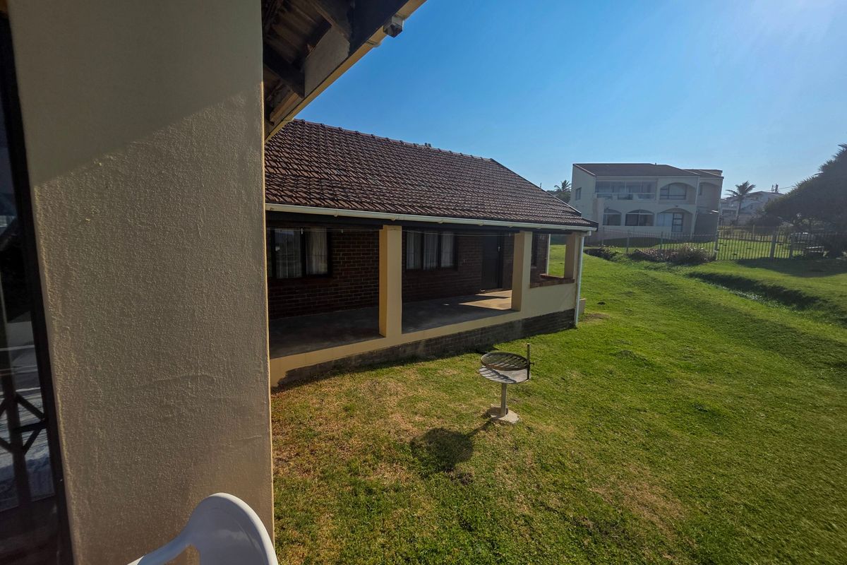 Rear view of the property featuring a covered patio, brick exterior walls, tiled roof, and a spacious lawn area.
