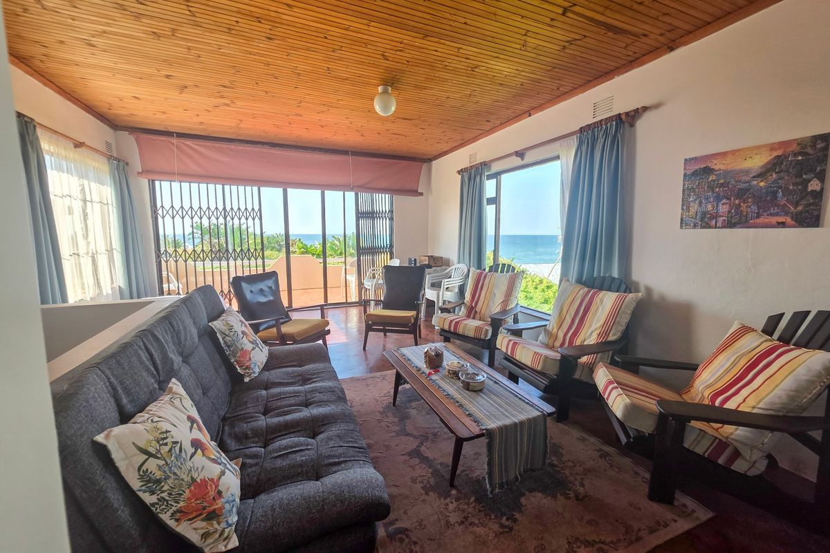 A living room featuring a timber-clad ceiling, large sliding doors with security gates, and direct views of the ocean.