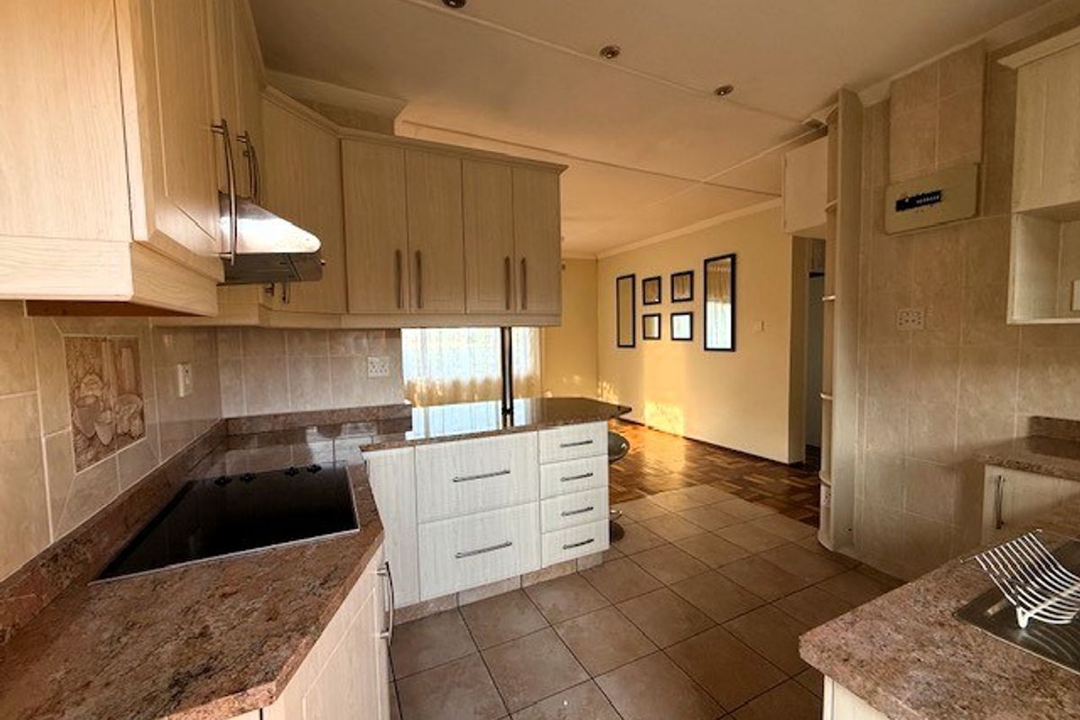 A functional kitchen featuring light wood cabinetry, granite countertops, an integrated electric hob with extractor fan, and tiled finishes throughout.