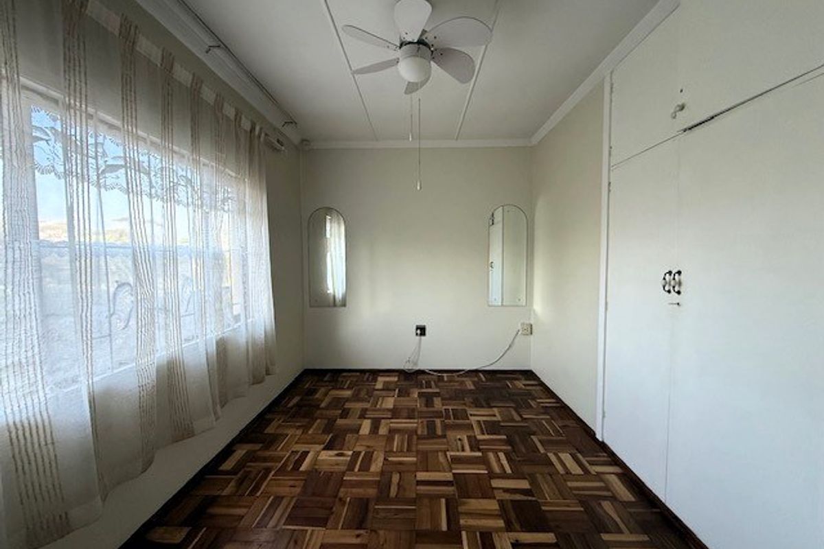 A bright, empty bedroom featuring classic parquet flooring, built-in storage cupboards, and a ceiling fan, offering a clean canvas for personalization.