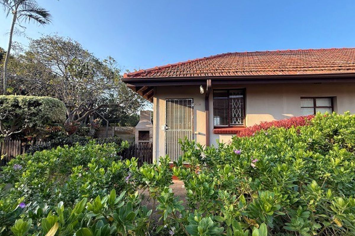 Rear view of the townhouse featuring a tiled roof, security-fitted windows and door, and a private garden area with a built-in braai.