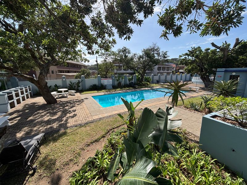 Communal outdoor pool area featuring a paved patio, established garden landscaping, and a built-in braai facility within a secure complex.