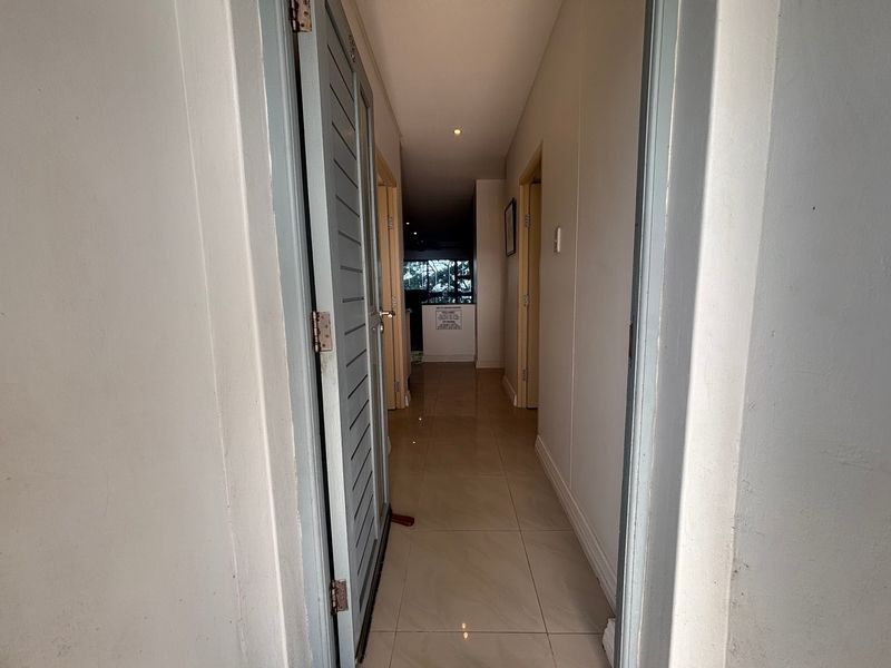 A clean, tiled hallway providing access to multiple rooms within the apartment, featuring neutral walls and recessed lighting.