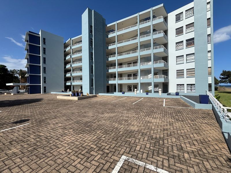 Exterior view of a multi-story apartment building featuring a paved parking area and private balconies for each unit.