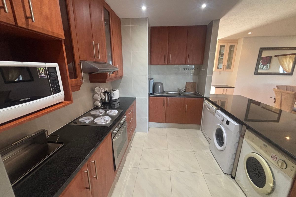 A functional kitchen featuring dark wood cabinetry, granite countertops, integrated appliances, and tiled flooring, with an open-plan layout connecting to the dining area.