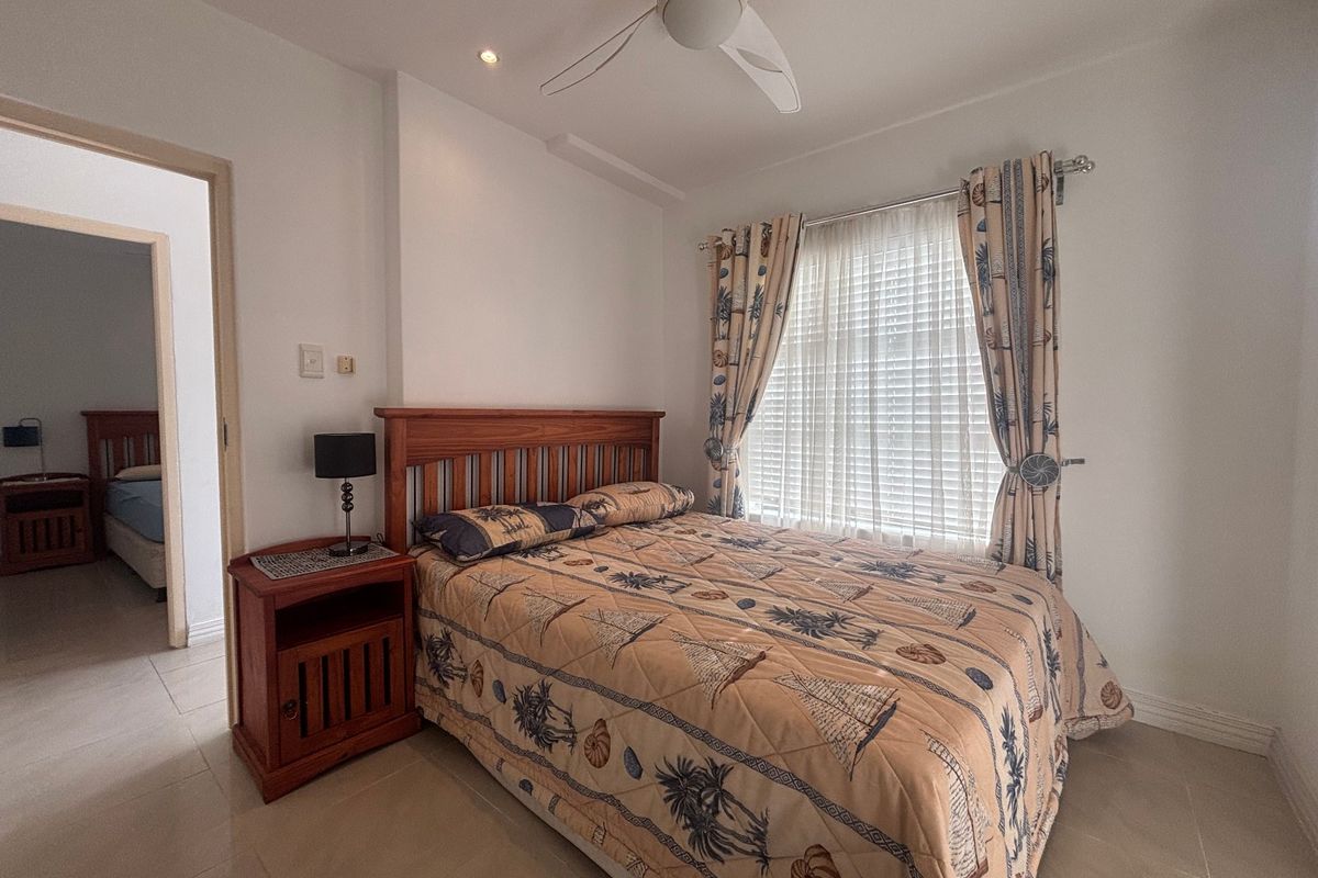 A well-maintained bedroom featuring tiled flooring, a ceiling fan, and recessed lighting, with an adjoining room visible through the doorway.