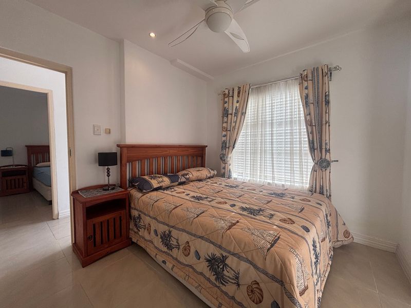 A well-maintained bedroom featuring tiled flooring, a ceiling fan, and recessed lighting, with an adjoining room visible through the doorway.