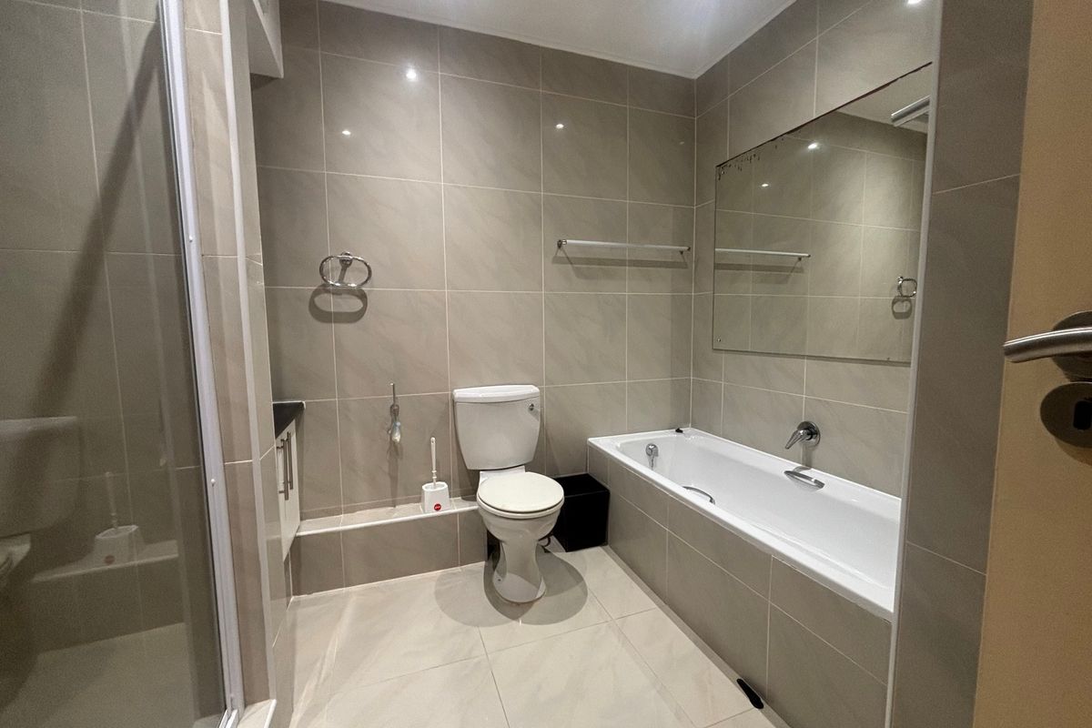 A modern, neutral-toned bathroom featuring a built-in bathtub, separate shower enclosure, and wall-mounted mirror with clean tiled finishes throughout.
