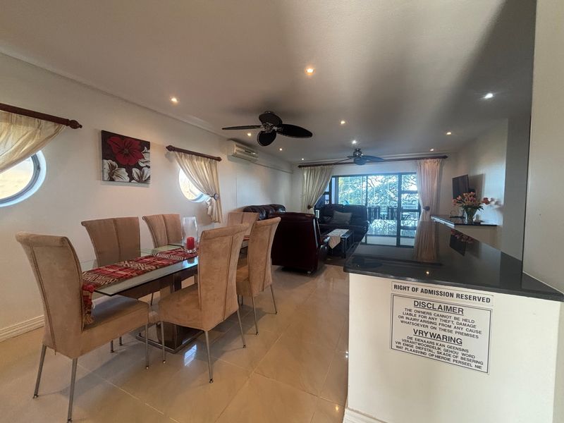 Spacious open-plan living and dining area featuring polished floor tiles, recessed lighting, ceiling fans, and a granite breakfast bar overlooking the lounge.