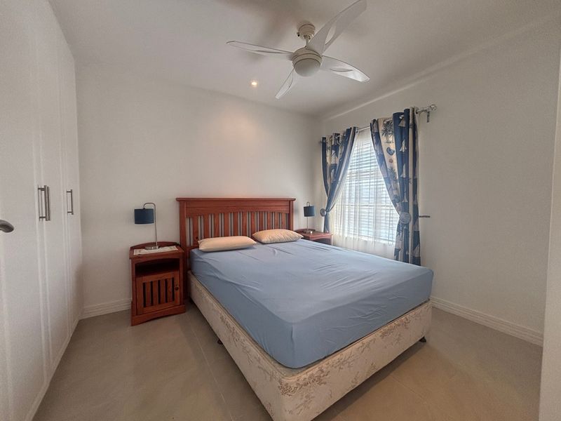 A well-maintained bedroom featuring neutral tiled flooring, a ceiling fan, and ample built-in wardrobe storage.