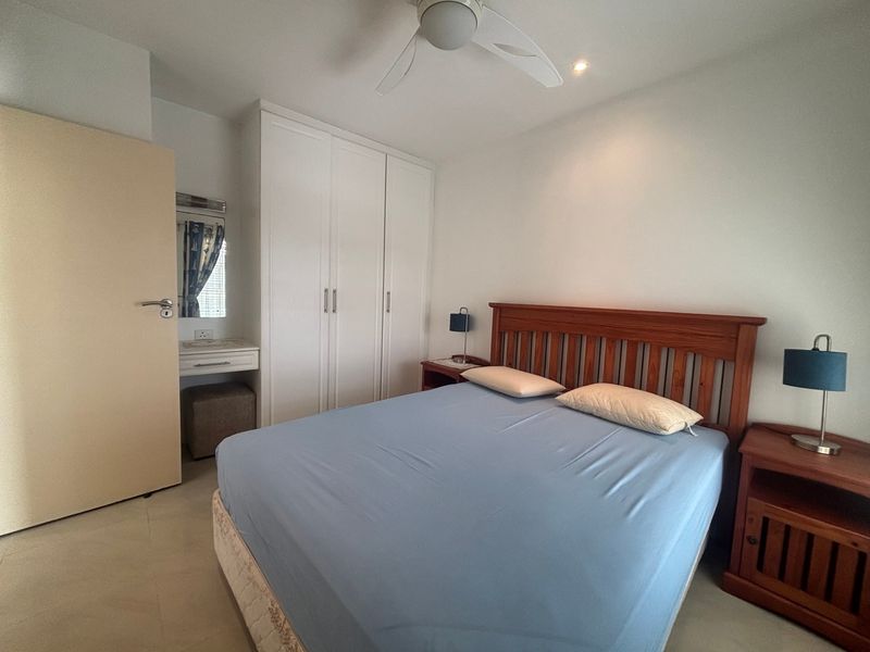A well-maintained bedroom featuring a built-in wardrobe, integrated vanity area, ceiling fan, and neutral tiled flooring.