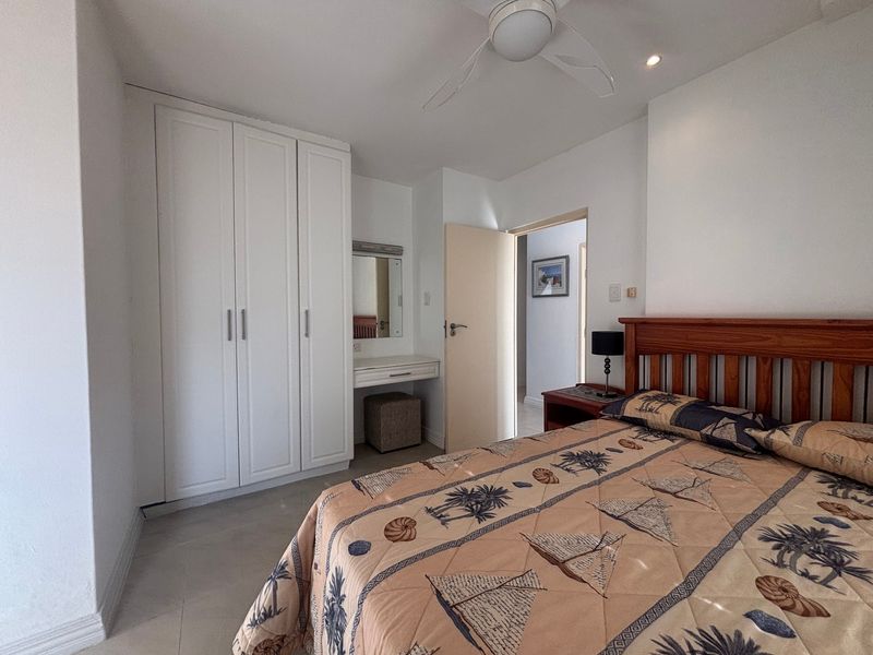 A well-maintained bedroom featuring built-in white cabinetry, a matching vanity area, and a ceiling fan, offering a clean and functional living space.