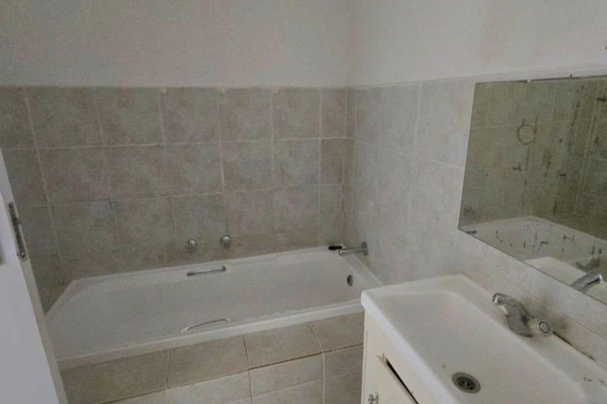 A functional bathroom featuring a built-in bathtub, vanity cabinet with basin, and tiled finishes, offering a blank canvas for modern renovation.