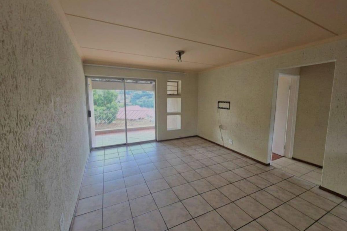 An empty living room featuring tiled flooring, textured walls, and a sliding glass door providing access to an outdoor area.