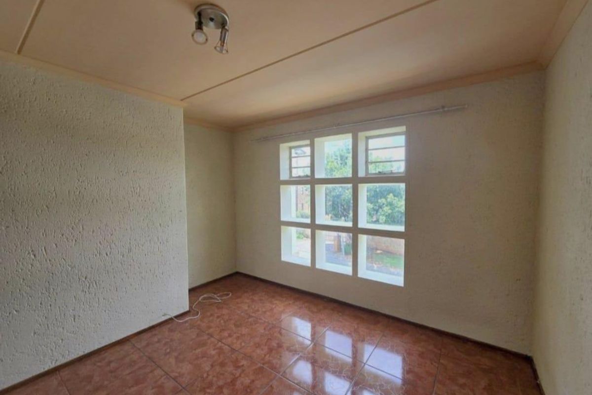 An empty bedroom featuring tiled flooring, textured walls, and a large grid-pattern window providing natural light.