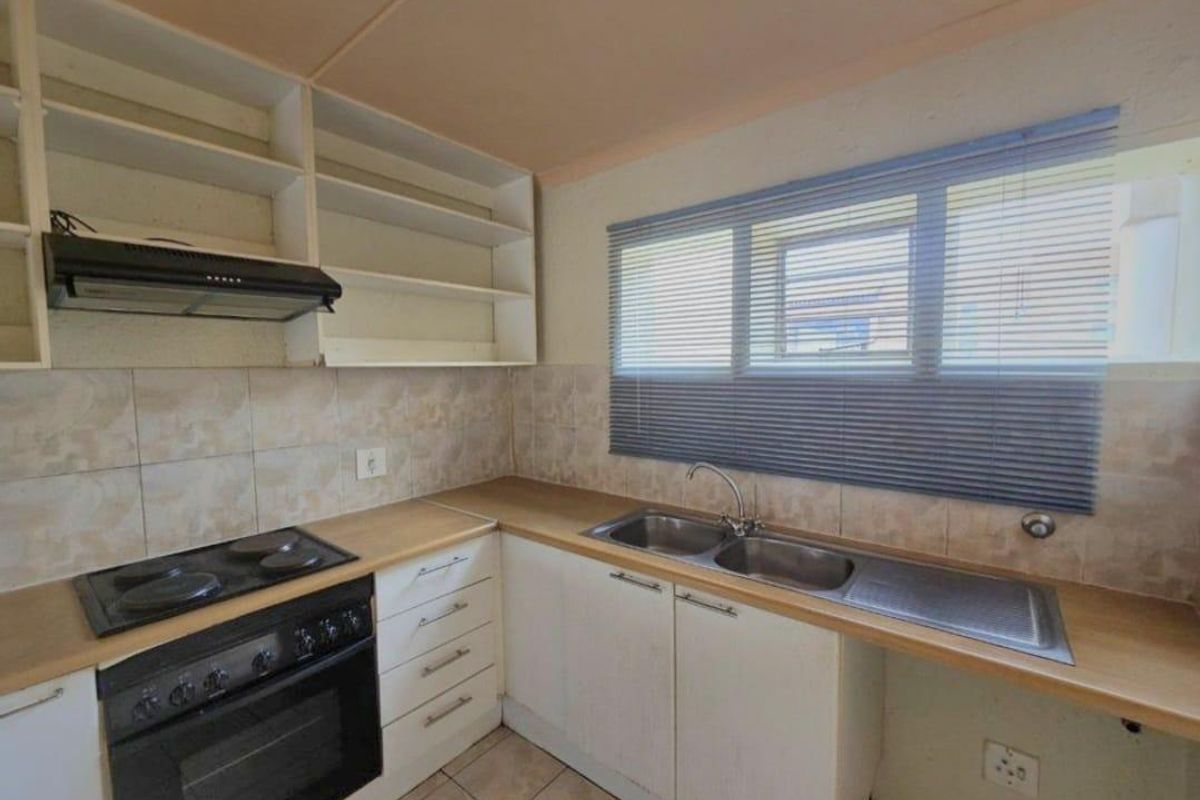 A functional kitchen featuring built-in oven, electric hob, extractor fan, double sink, and ample laminate countertop space with open shelving.