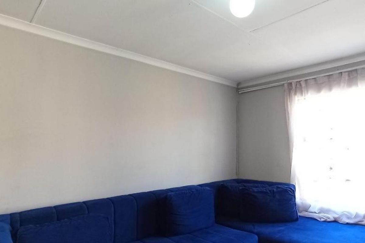 A simple living room featuring neutral walls, coving, and a large window with a curtain rail.
