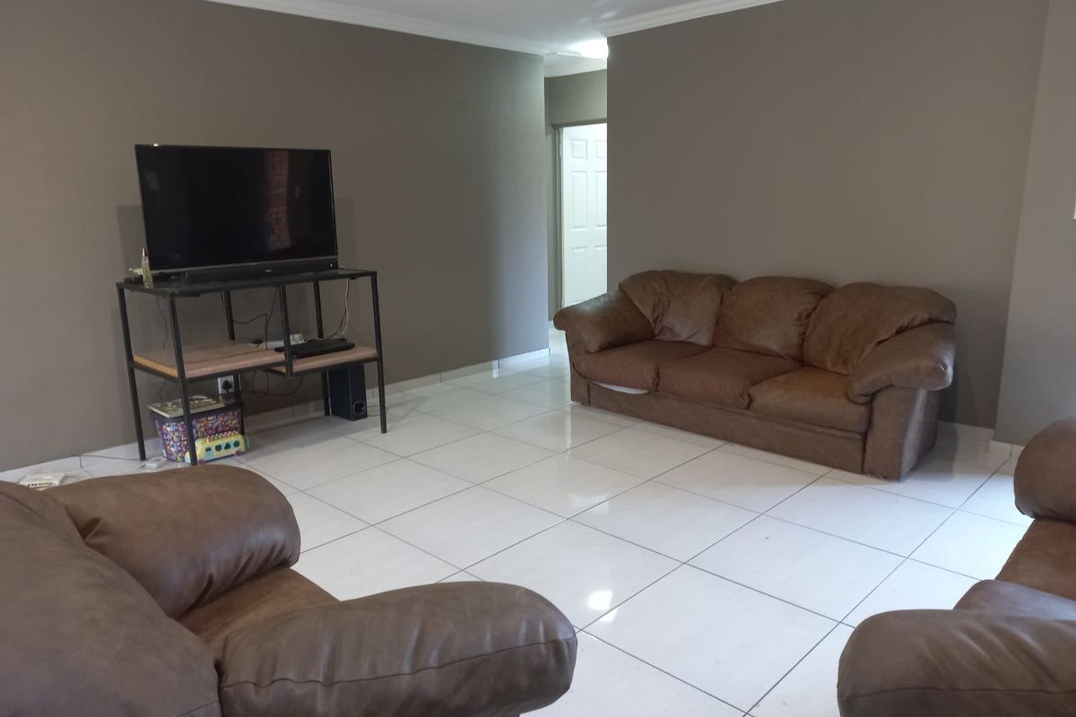 A spacious living room featuring neutral wall tones, large format floor tiles, and recessed ceiling lighting.