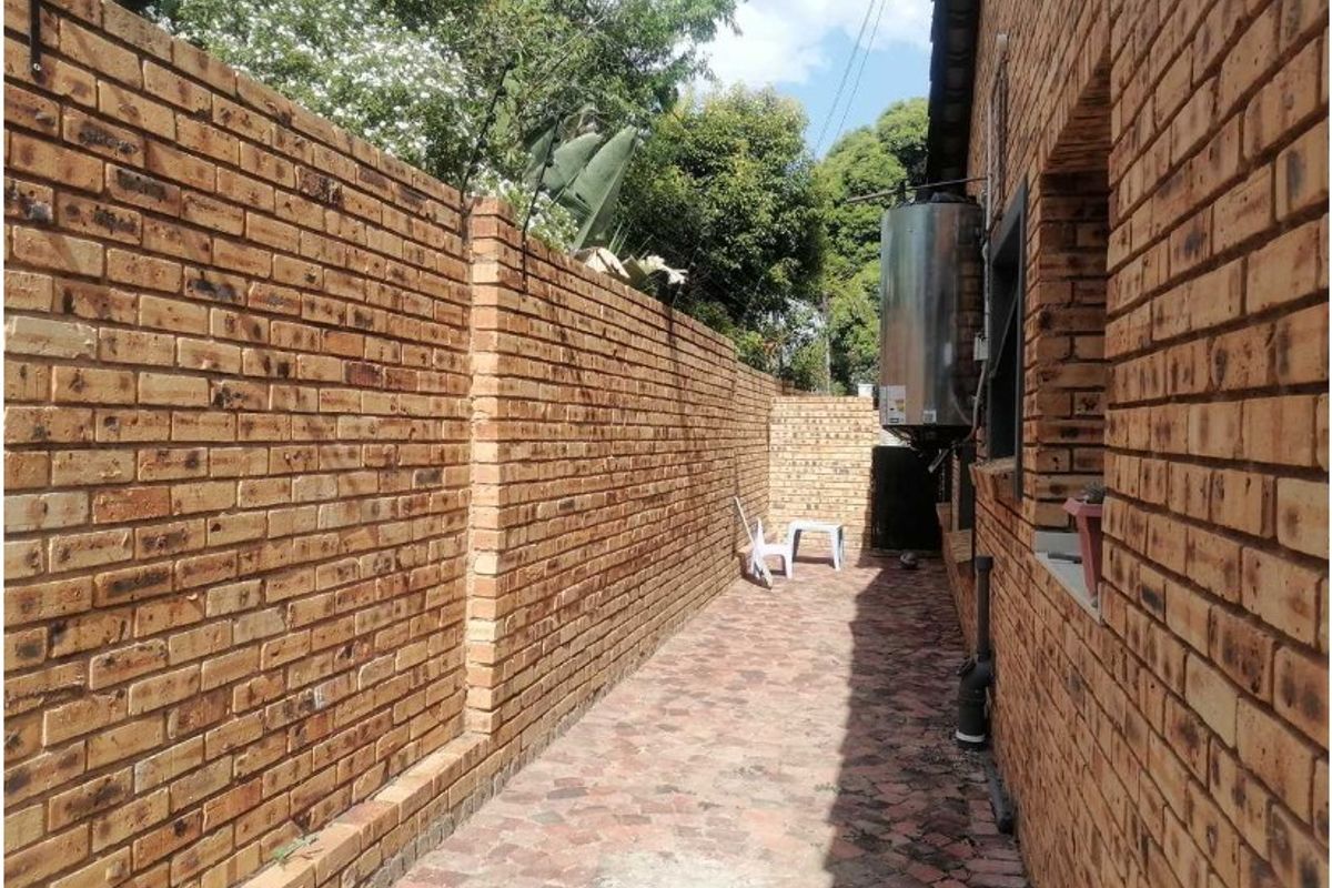 A side exterior walkway featuring face brick walls, paved flooring, and an external geyser unit.