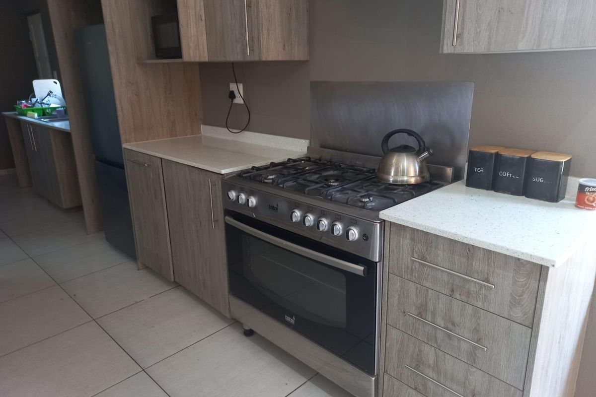 Modern kitchen featuring wood-grain cabinetry, stone countertops, and a stainless steel gas stove with matching splashback, complemented by neutral tiled flooring.
