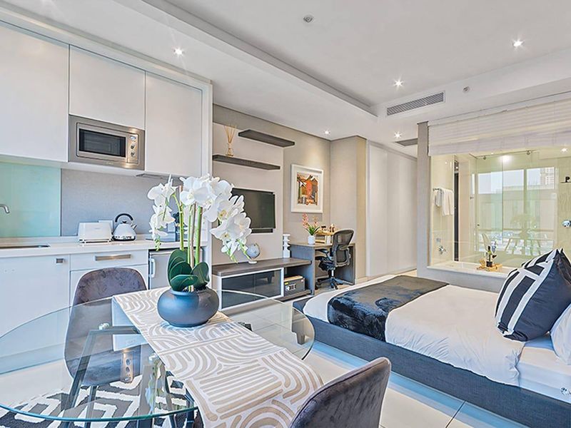 Modern open-plan studio apartment featuring a sleek kitchenette, integrated appliances, recessed lighting, and a contemporary glass-enclosed bathroom suite.