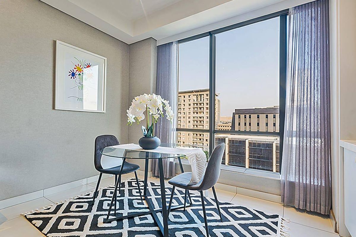 A bright dining area featuring floor-to-ceiling windows with urban views, neutral wall finishes, and modern tiled flooring.