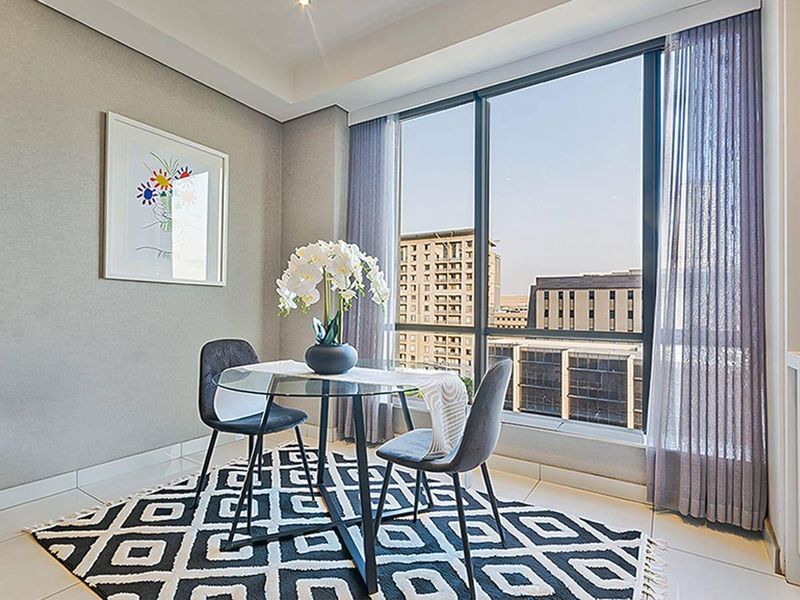 A bright dining area featuring floor-to-ceiling windows with urban views, neutral wall finishes, and modern tiled flooring.
