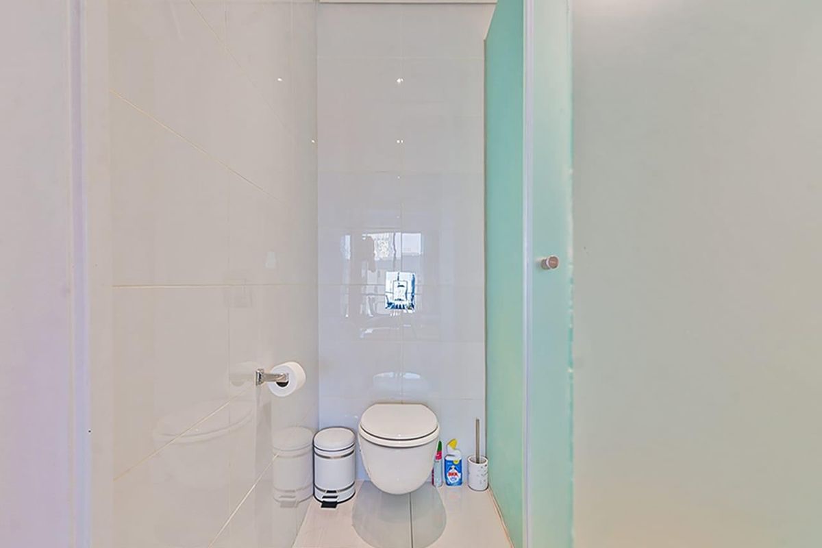 A compact, modern bathroom featuring a wall-mounted toilet, white ceramic tiling, and a frosted glass privacy screen.