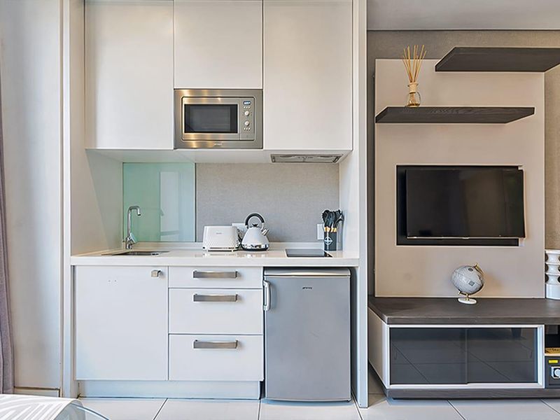 Compact open-plan kitchenette featuring modern white cabinetry, built-in microwave, and integrated hob, adjacent to a custom media unit with built-in shelving.