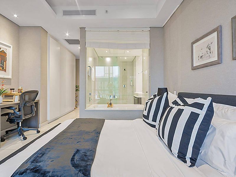 Modern bedroom featuring a glass-enclosed ensuite bathroom, built-in wardrobes, recessed ceiling lighting, and neutral finishes throughout.