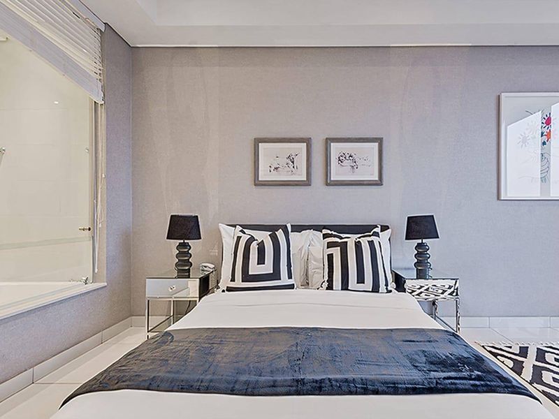Modern bedroom featuring a glass partition wall, recessed ceiling lighting, and sleek tiled flooring in a well-maintained contemporary apartment.