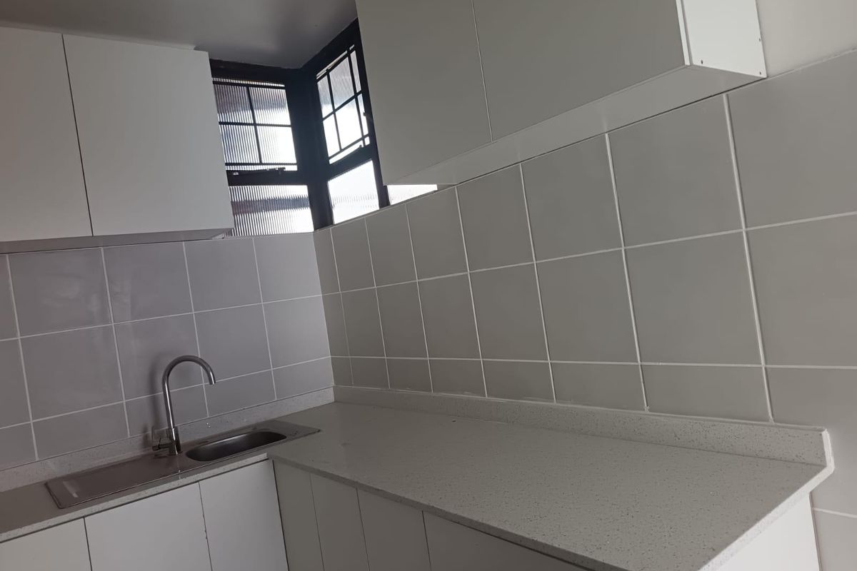 A clean, modern kitchen featuring white cabinetry, stone countertops, a stainless steel sink, and a tiled splashback.