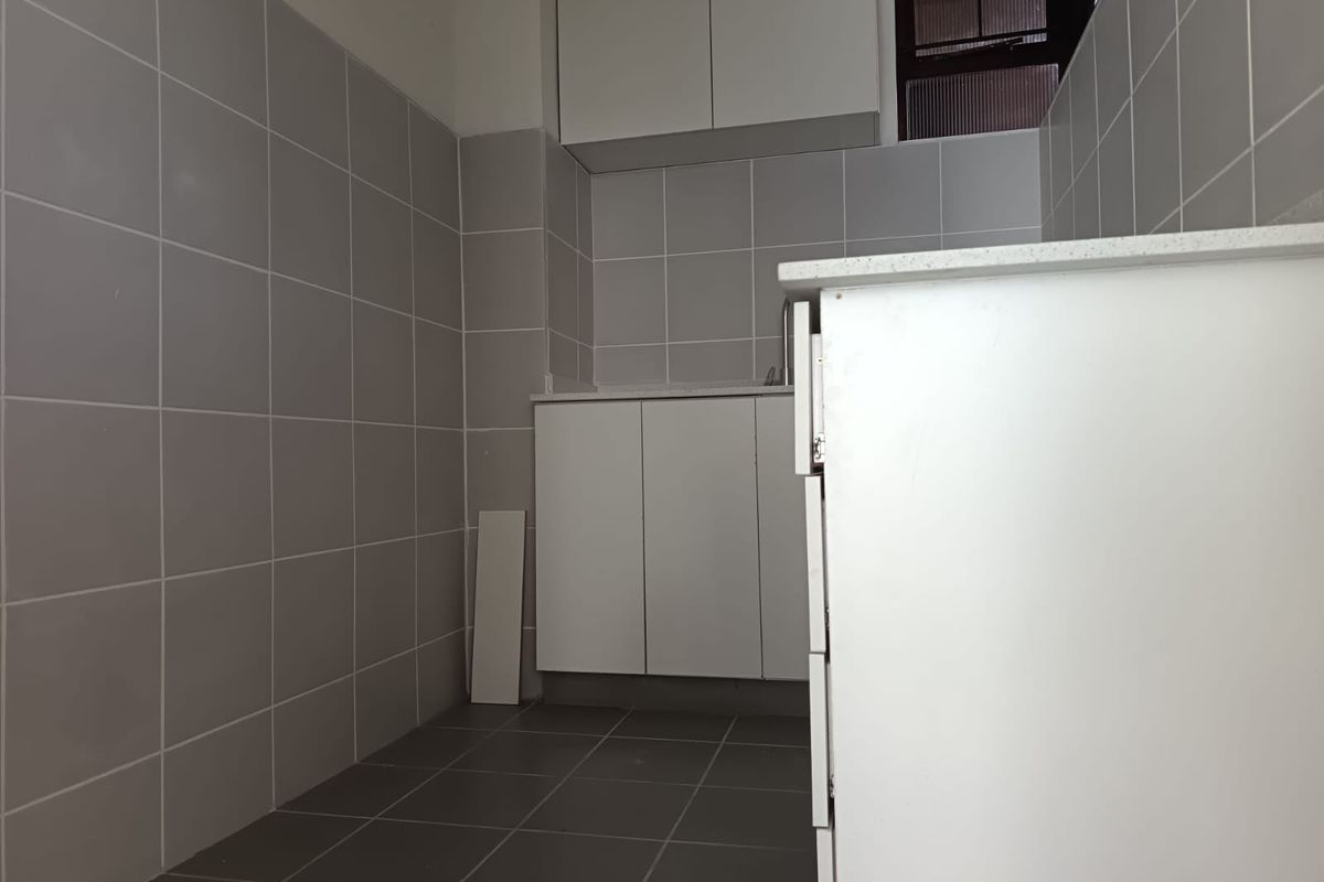 A compact, empty kitchen featuring neutral grey wall and floor tiles, white built-in cabinetry, and stone countertops, awaiting final finishing touches.