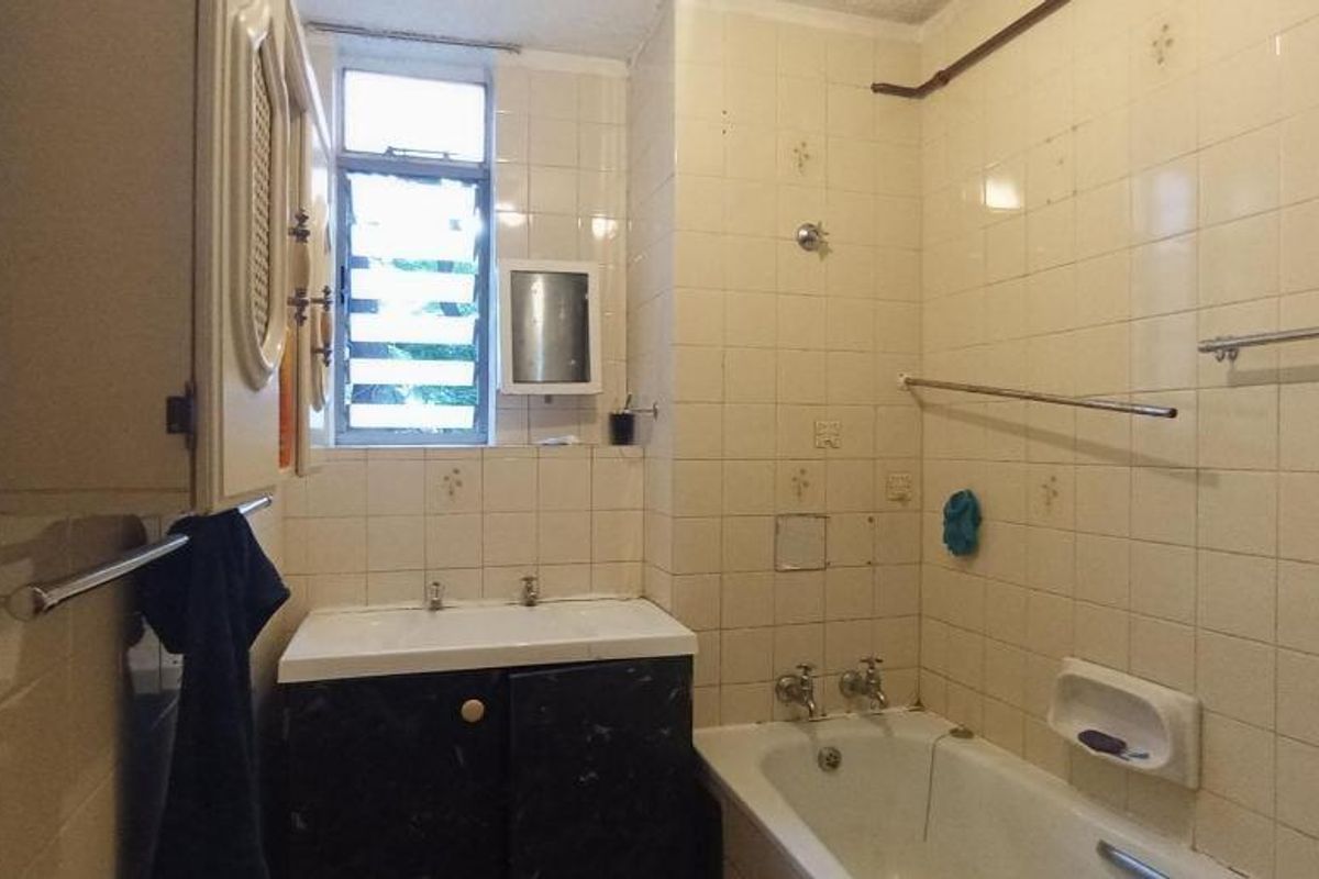 A dated bathroom featuring a built-in vanity, bathtub, and tiled walls, offering significant potential for a modern renovation.