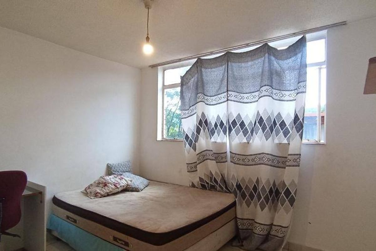 A simple bedroom featuring a large window providing natural light and a basic pendant light fixture.