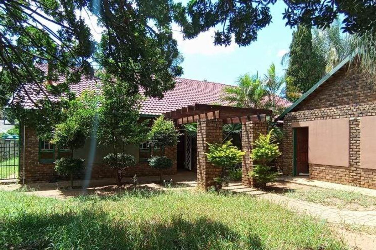 Rear view of the property featuring a brick facade, tiled roof, and a wooden pergola structure set within a garden area.