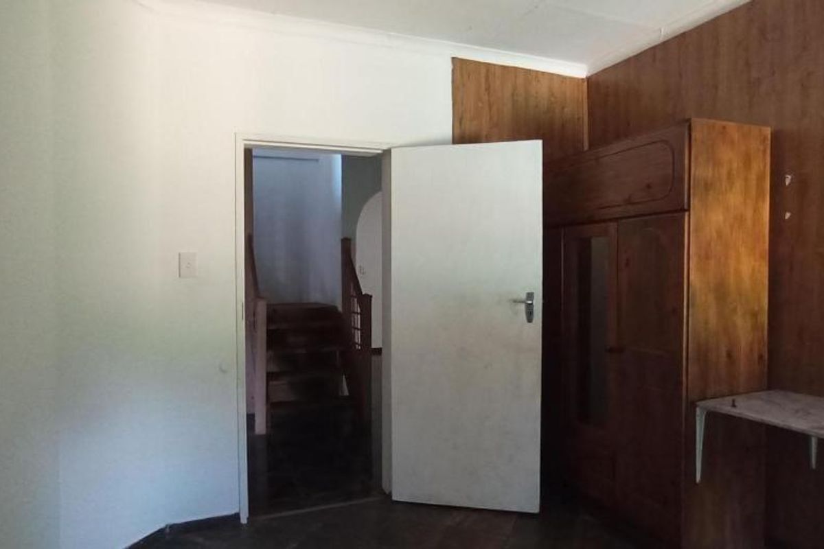 A bedroom featuring dated wooden wall paneling and a built-in wardrobe, with an open doorway leading to a staircase.