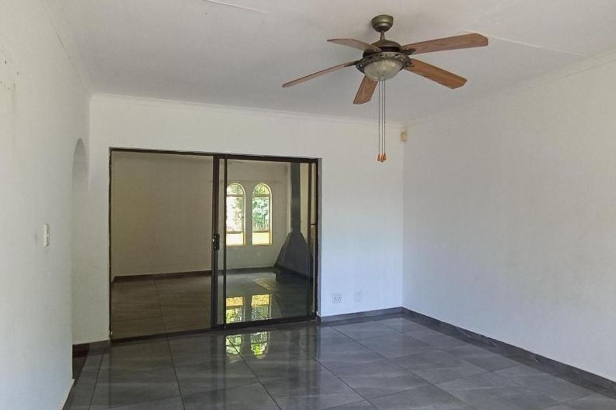 A spacious, empty living area featuring tiled flooring, a ceiling fan, and sliding glass doors leading to an adjacent room.