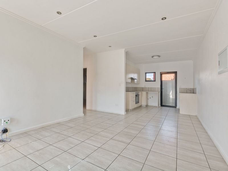 An open-plan living and kitchen area featuring tiled flooring, recessed lighting, and functional built-in cabinetry with integrated appliances.