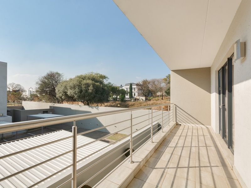 A clean, modern balcony featuring tiled flooring, a stainless steel balustrade, and a sliding glass door, offering an open view of the surrounding area.