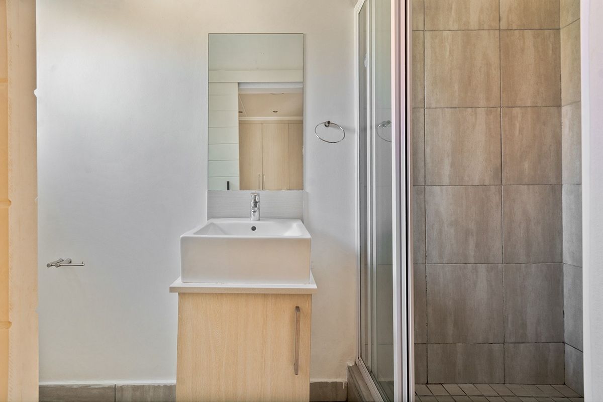A clean, modern bathroom featuring a vessel sink vanity, wall-mounted mirror, and a tiled shower enclosure with a glass door.