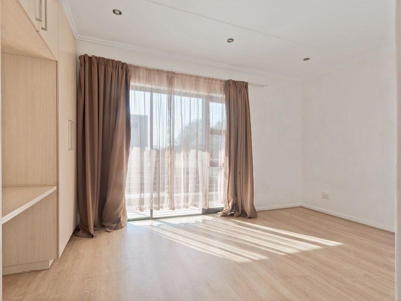 A bright, empty bedroom featuring light wood-look laminate flooring, built-in cupboards, and a sliding glass door leading to an outdoor area.